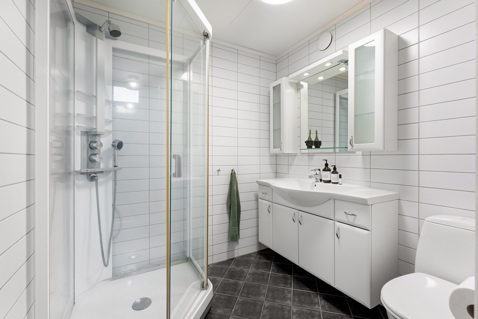 Flislagt bad med varmekabler i underetasjen. Rommet har innredning med nedfelt servant, veggskap, speil, toalett og lukket dusjkabinett. Galleribilde