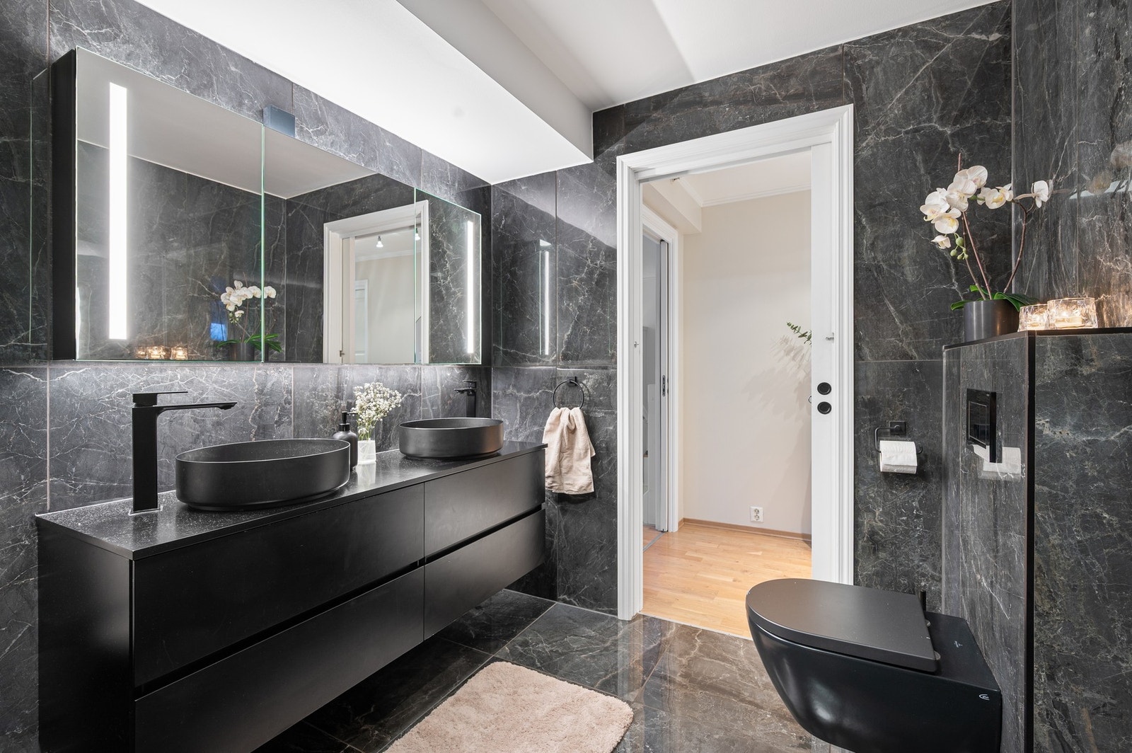 Moderne bad innredet med dobbel servant og stort speilskap, vegghengt toalett, stor dusjnisje med foldedør og regndusj. Stilig og praktisk løsning skjult bak skyvedør, for vaskemaskin og tørketrommel. Galleribilde