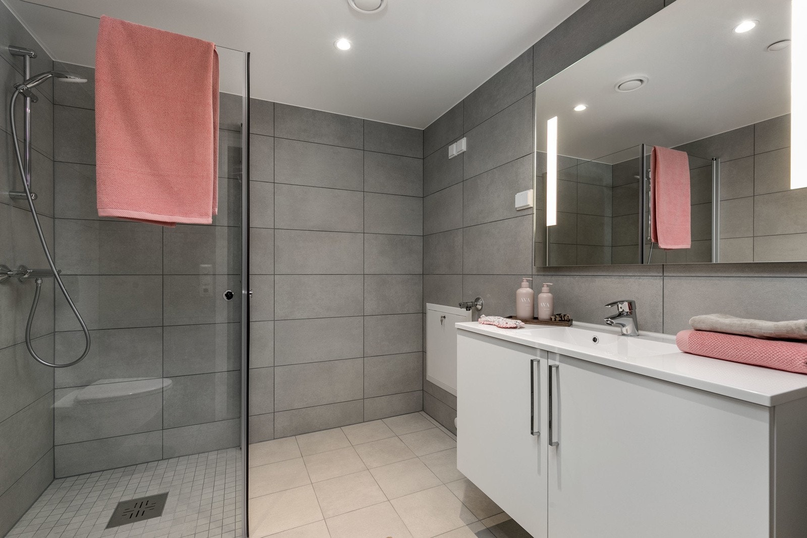 Delikat flislagt bad med vegghengt toalett, dusjsone med innfellbare dører samt servant med skapinnredning. Galleribilde