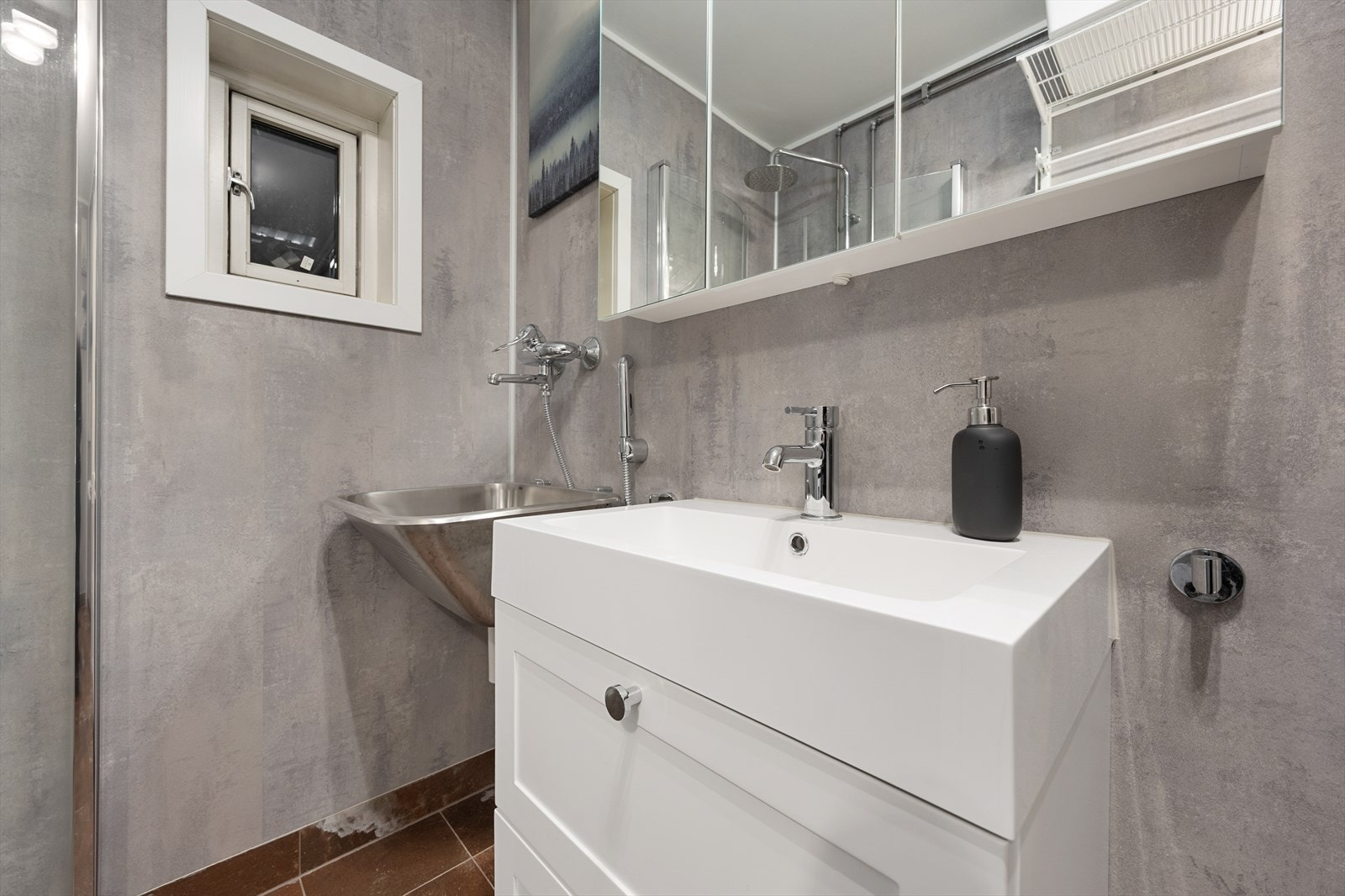 Baderommet inneholder servantseksjon med skuffer, vegghengt klosett, opplegg for vaskemaskin og dusjhjørne. Galleribilde