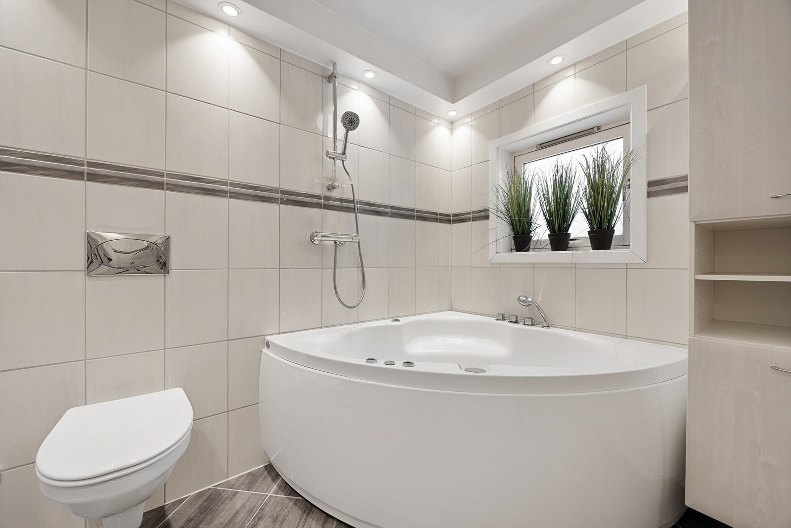 Badet inneholder stort badekar, veggmontert klosett og servantseksjon. Galleribilde