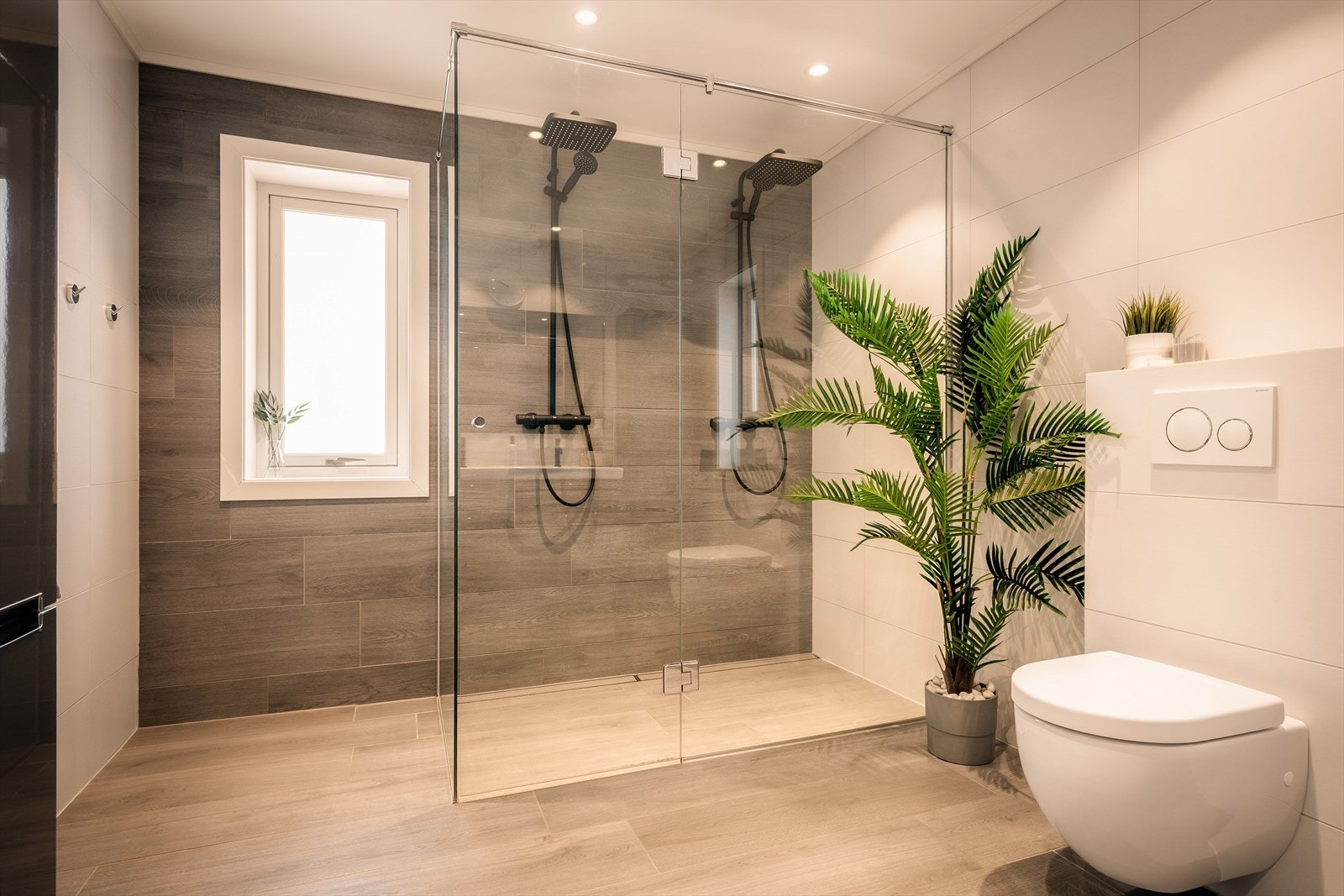 Lekkert og moderne baderom med store, elegante fliser som gir et stilrent og eksklusivt uttrykk. Den doble regnsfallsdusjen med gjennomgående sort armatur skaper en luksuriøs spa-følelse. Galleribilde