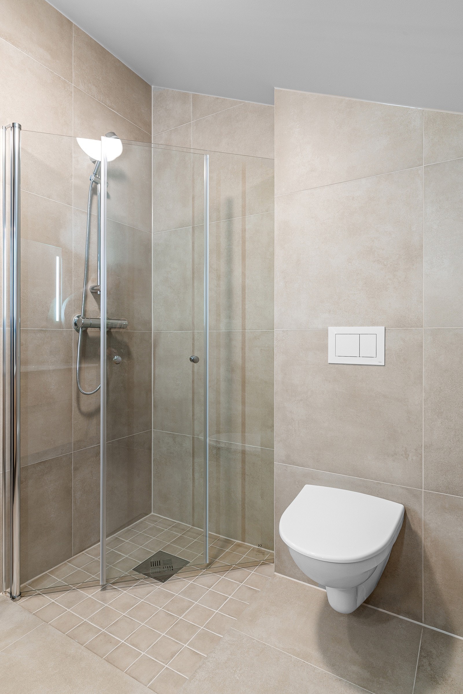 Videre er badet utstyrt med servant på skuffeseksjon, speil med belysning, vegghengt toalett og innfellbare dusjdører. Galleribilde