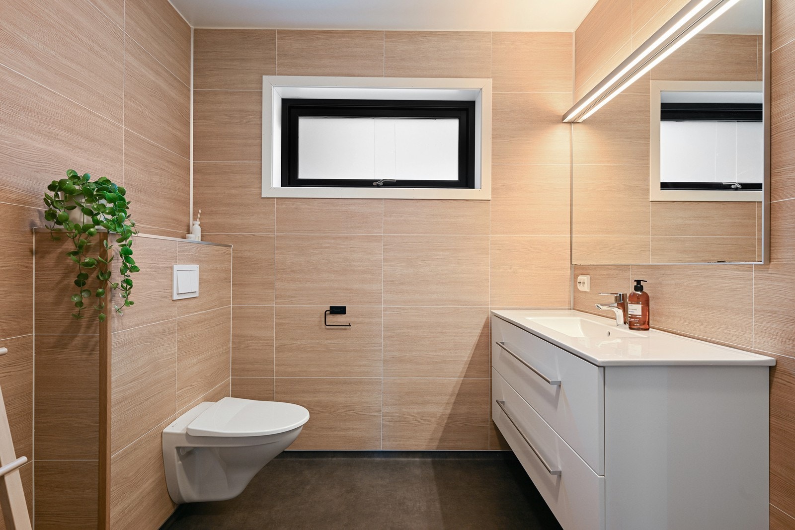 Moderne bad i varme toner, vegghengt toalett, servantinnredning med speil og belysning samt dusj med innfellbare glassdører. Galleribilde