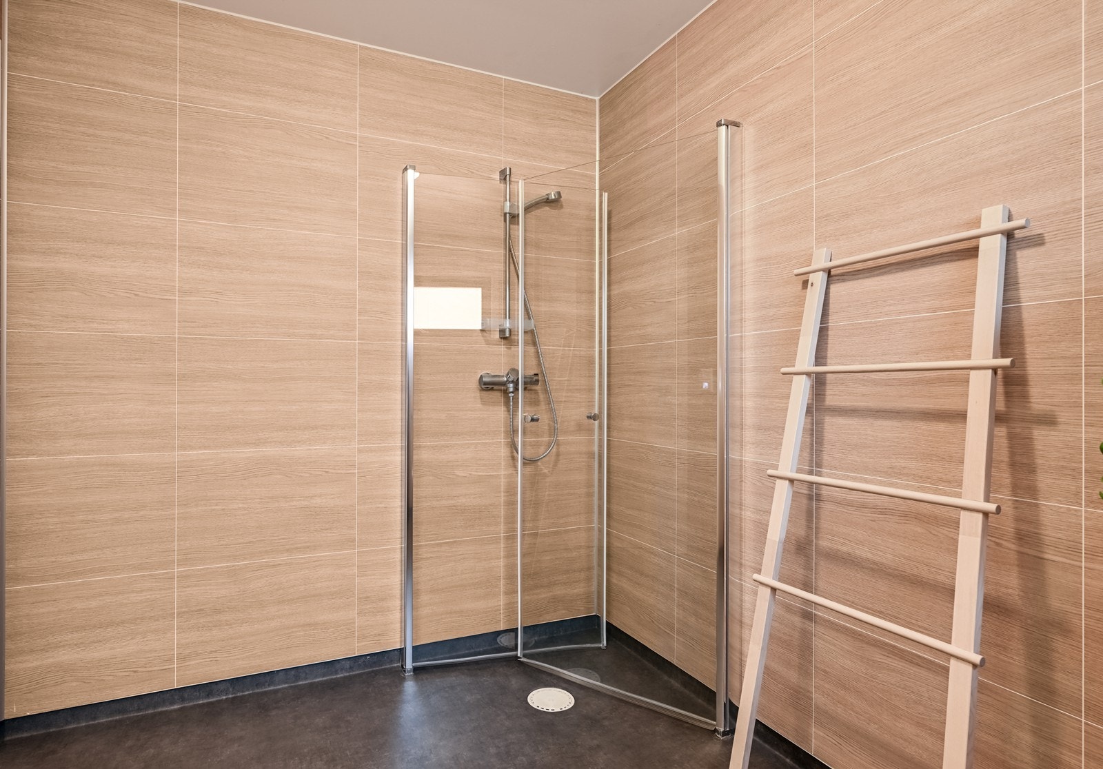 Moderne bad i varme toner, vegghengt toalett, servantinnredning med speil og belysning samt dusj med innfellbare glassdører. Galleribilde