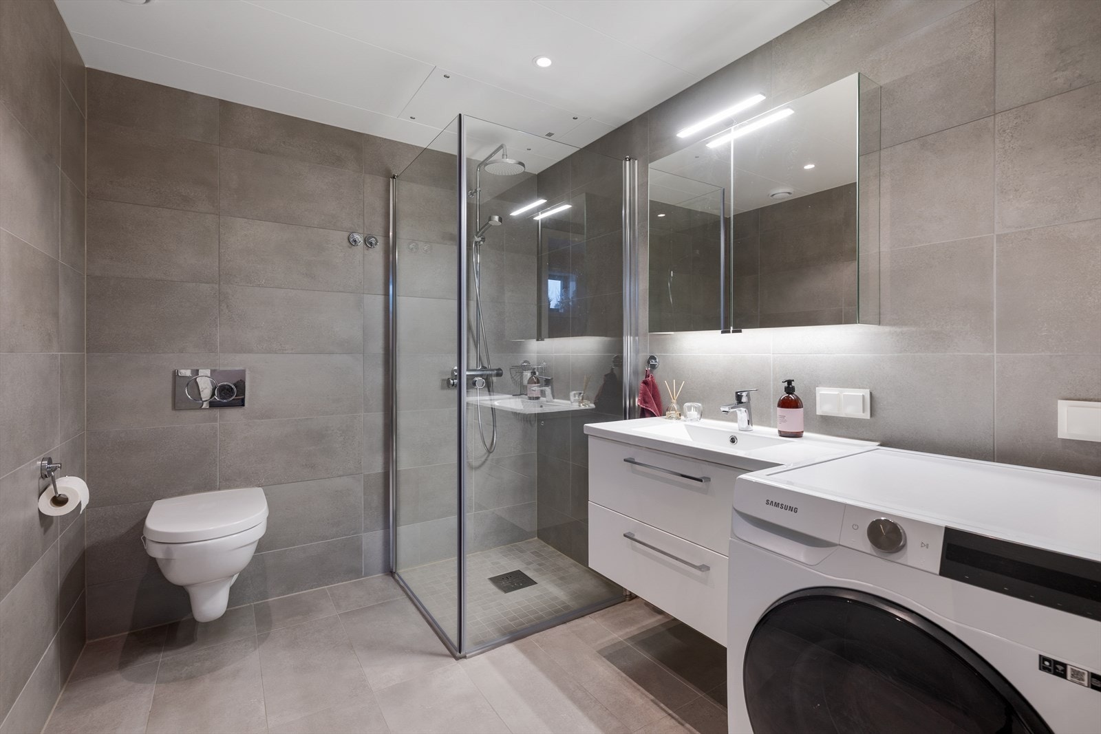 Stilrent og moderne flislagt bad med dusjnisje, vegghengt wc, pen innredning m/vask og opplegg for vaskemaskin. Galleribilde