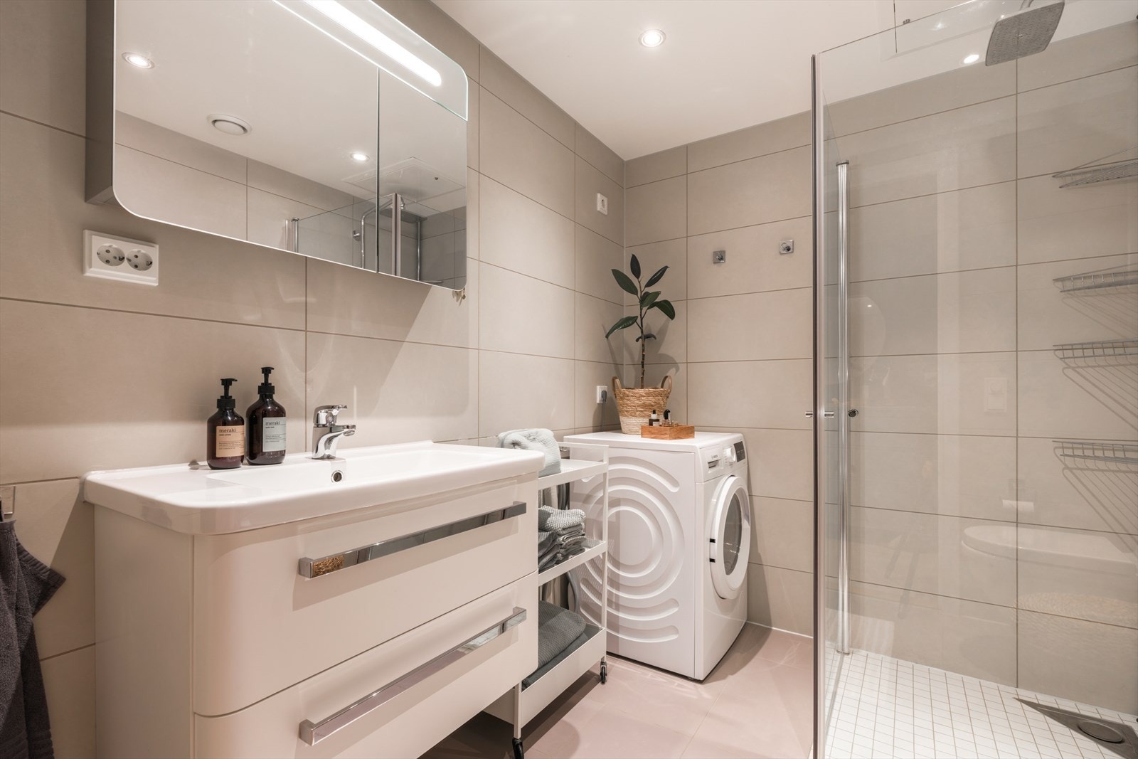 Moderne baderomsinnredning med skuffer og heldekkende servant, speilskap med belysning over, samt vegghent toalett med soft close. Plass til vaskemaskin og tørketrommel. Galleribilde