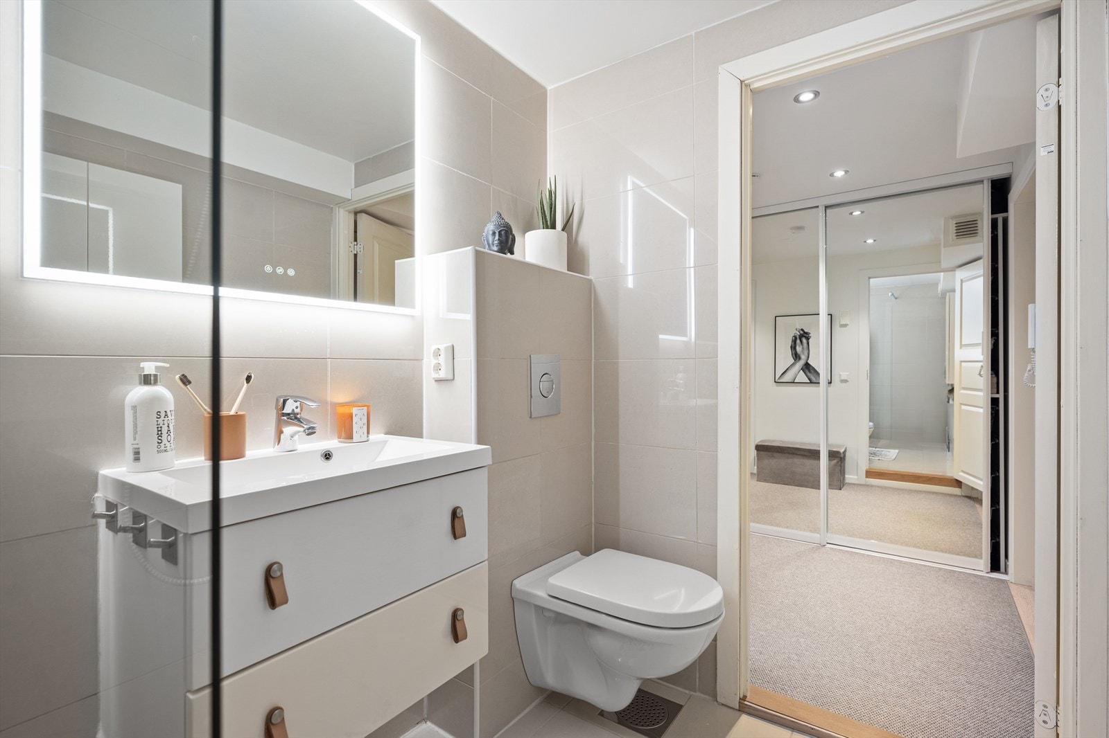 Badet er flislagt med elektriske varmekabler i gulvet. Rommet er innredet med nedfelt servant og glatte fronter, veggmontert toalett og dusj på gulv. Galleribilde