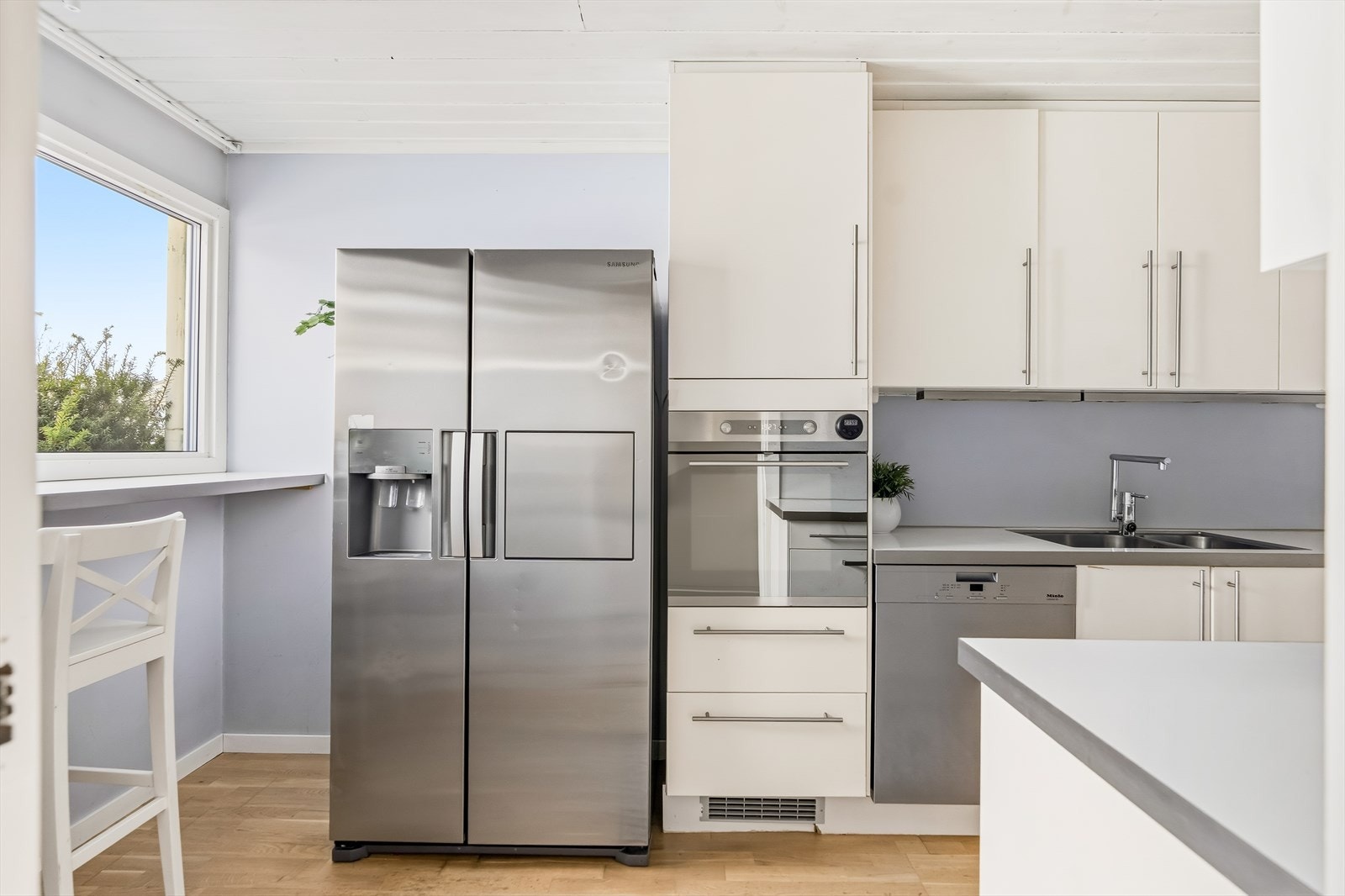 Integrerte hvitevarer som ventilator, platetopp og stekeovn. Oppvaskmaskin og side-by-side kjøleskap med frysedel er plassert i nisjer og medfølger. Galleribilde