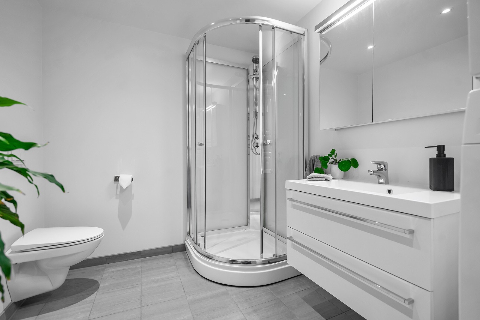 Lyst og moderne bad med fliser på gulv, dusjkabinett, vegghengt toalett og opplegg for vaskemaskin. Galleribilde