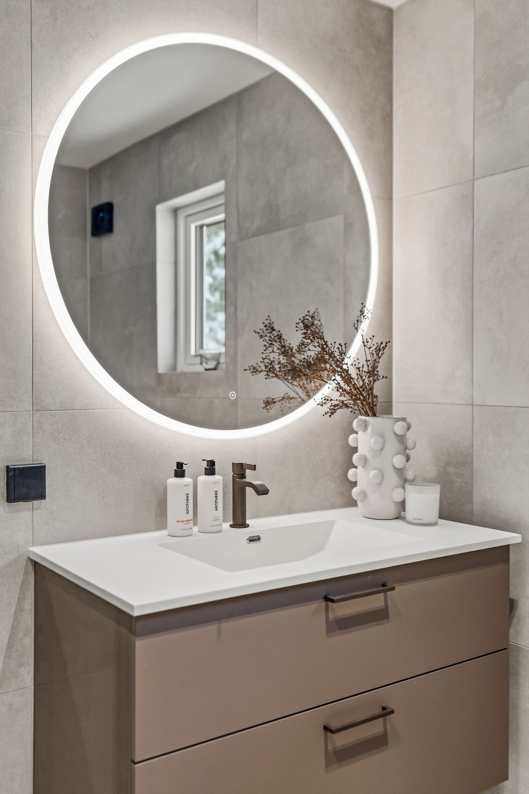 Videre er det montert servantskap med glatte, folierte fronter og heldekkende servant, speilskap med lysarmatur på vegg over servant samt et veggmontert toalett. Galleribilde