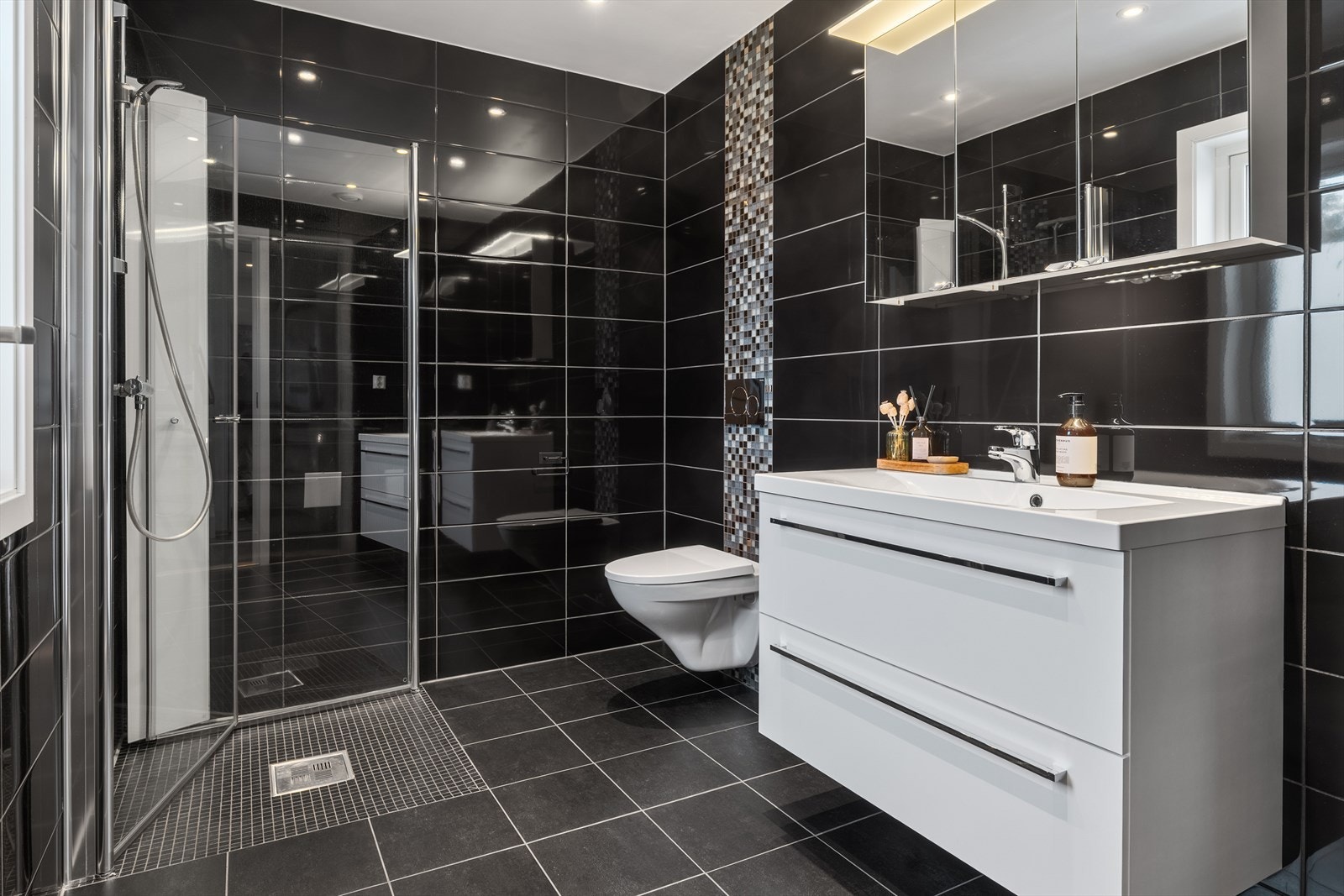 Rommet er innredet med dusj med glassvegger, servant med tilhørende innredning som gir gode oppbevaringsmuligheter, samt speil med integrert belysning. Vegghengt toalett bidrar til et ryddig og lettstelt uttrykk. Galleribilde