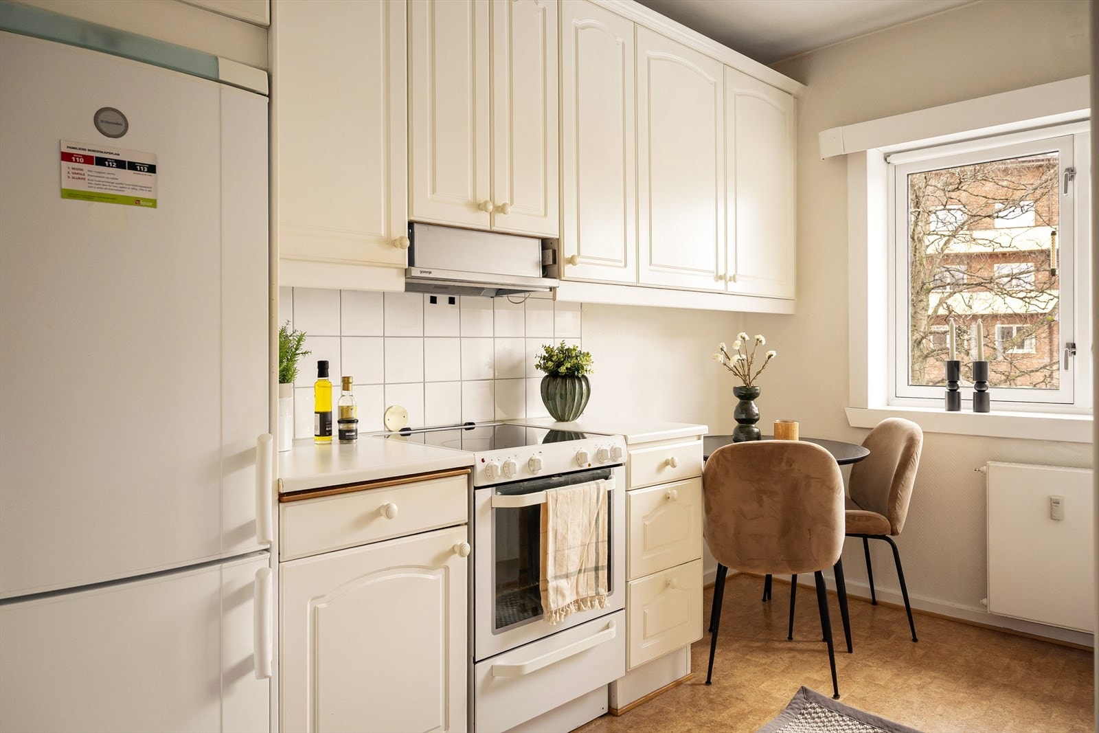 Kjøkkeninnredningen med hvite, profilerte fronter, fliser på vegg over kjøkkenbenk og benkeplate i laminat. Galleribilde