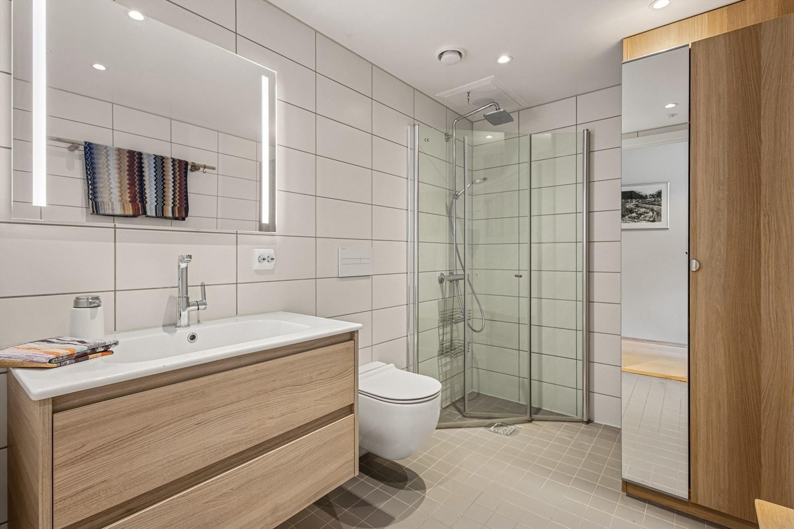 Ved kjøp ble badekabin oppgradert som tilvalg. Boligens bad har flislagte overflater på både vegger og gulv. Det er behagelig vannbåren gulvvarme og innfelte downlights i det malte taket. Galleribilde