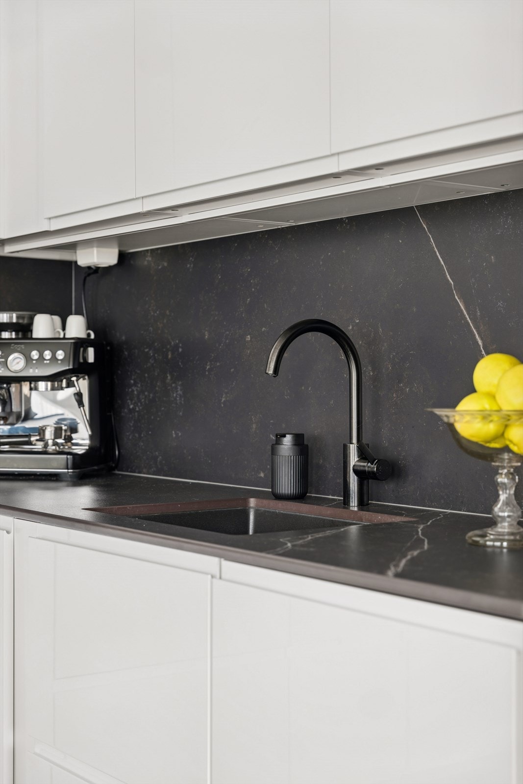 De glansede, hvite frontene gir et rent og elegant uttrykk, mens den mørke eksklusive keramikkbenkeplaten og bakveggen tilfører en stilig kontrast som gir rommet et eksklusivt preg. Galleribilde