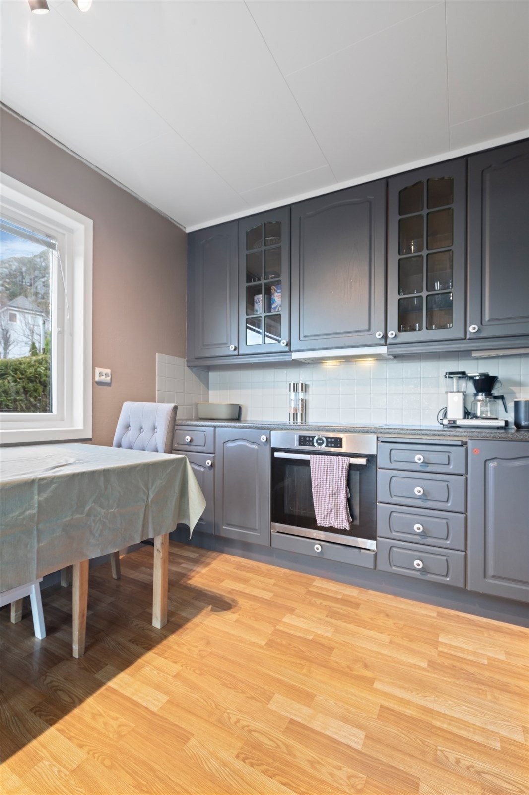 Kjøkkenet har innredning med profilerte, malte skapfronter og med glass, og med takhøye overskap | benkeplater av laminat med nedfelt vask og platetopp | integrert komfyr og ventilator, og utsparing for oppvaskmaskin og kjøleskap Galleribilde