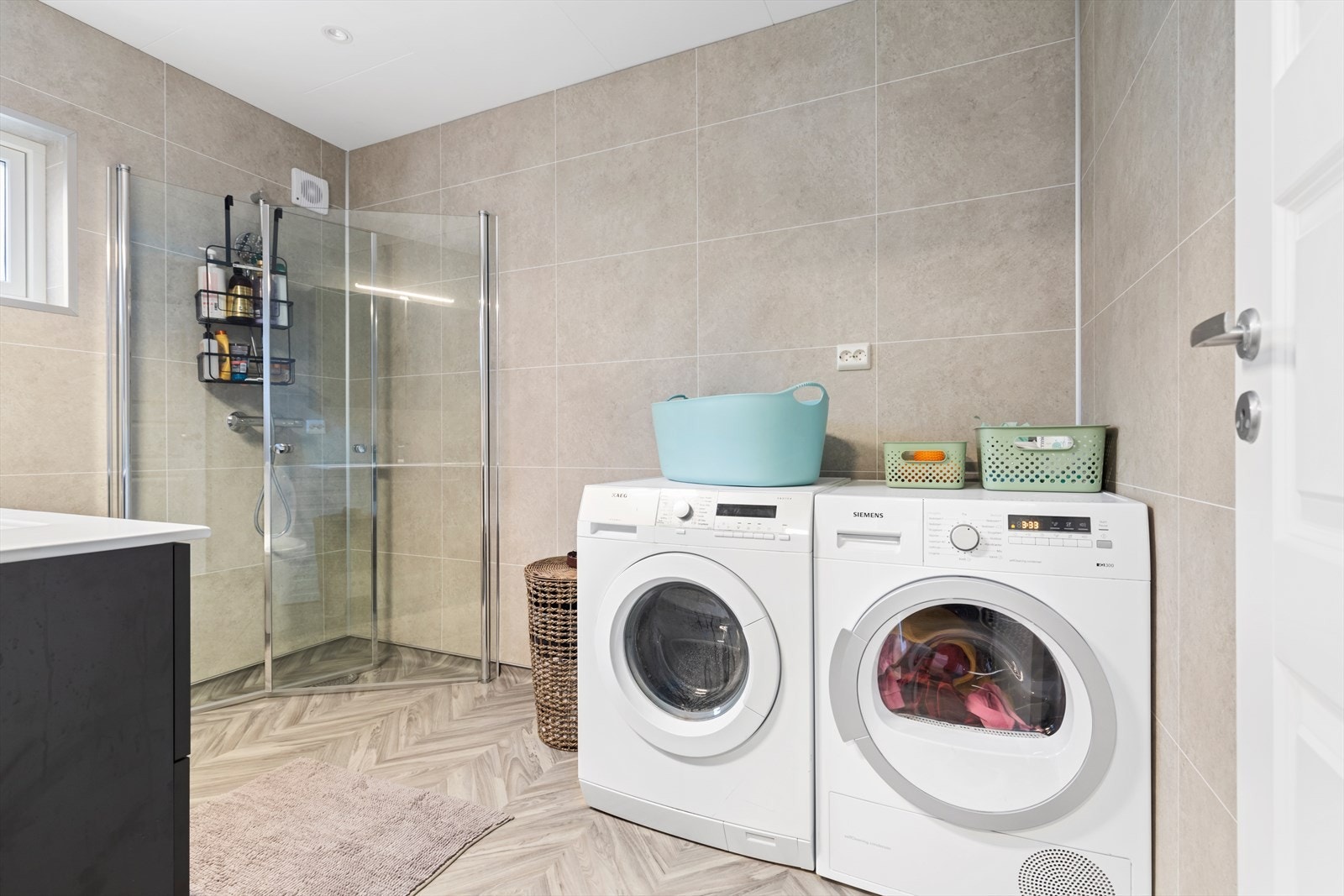 Bad/vaskerom i hovedetasjen ble renovert i 2025 | badet har vinylbelegg med oppkant på gulv og våtromsplater på vegger | rommet er utstyrt med baderomsinnredning, vegghengt dusj med dusjvegger, wc og opplegg for vaskemaskin og tørketrommel Galleribilde