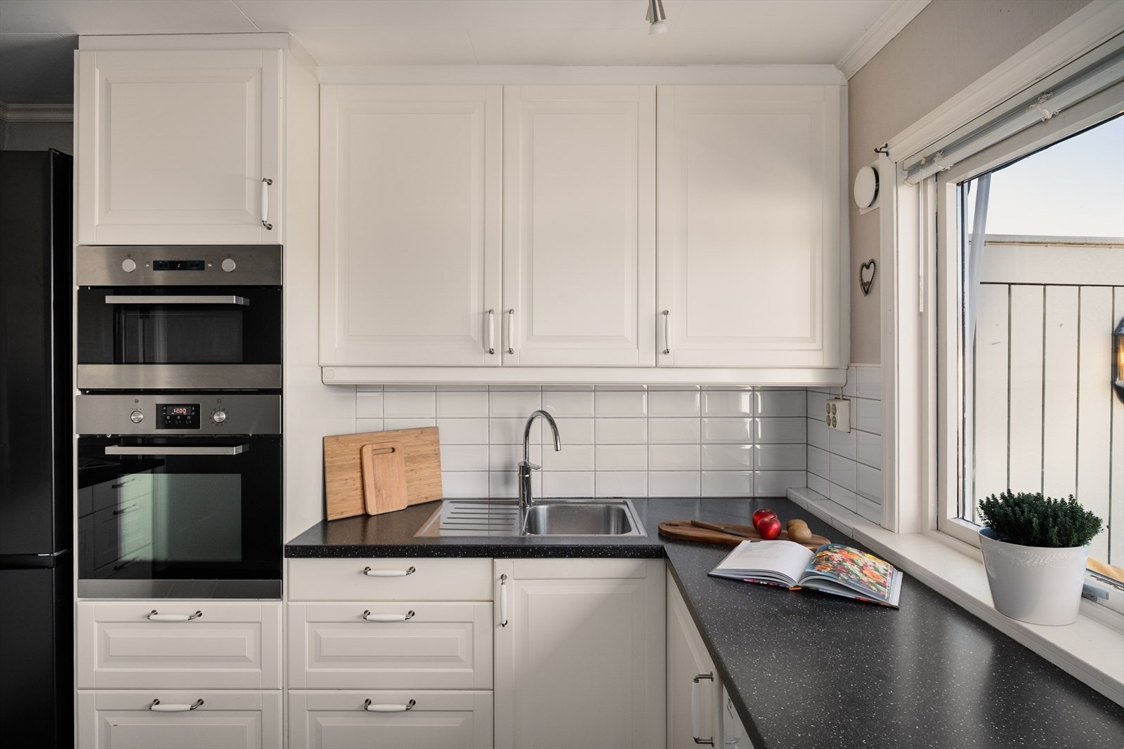 Kjøkkenet er innredet med profilerte hvite fronter, laminert benkeplate, fliser over benkeplaten og praktiske overskap til tak. Galleribilde