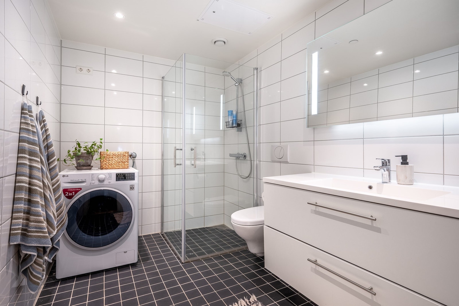 Moderne, helfliset bad med behagelig gulvvarme, innredet med vegghengt toalett, servant med innredning, dusjhjørne med glassdører og opplegg for vaskemaskin. Galleribilde