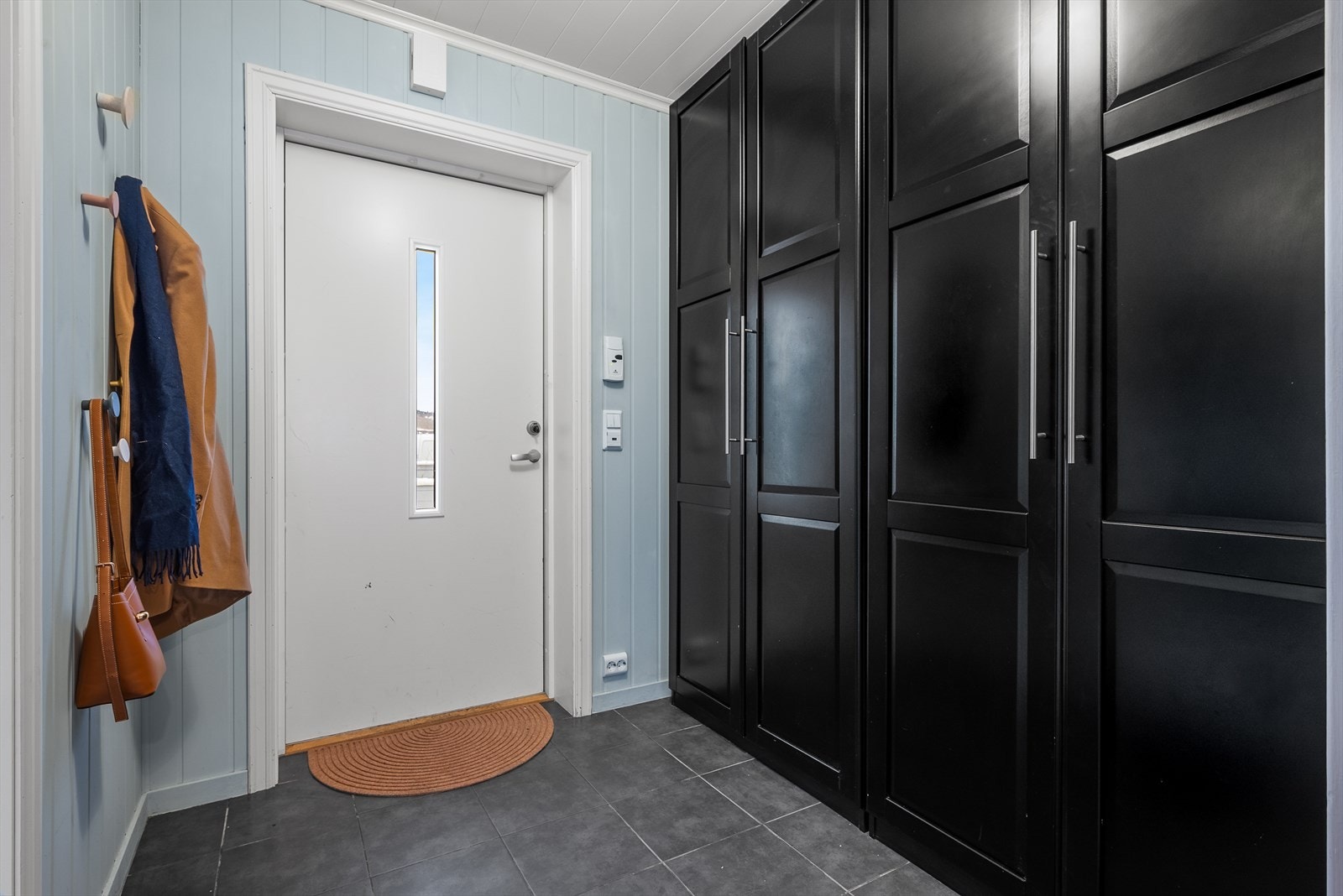 Boligens innbydende entré på 5m², har godt med plass til både yttertøy og sko i et stilrent og praktisk garderobeskap. Galleribilde