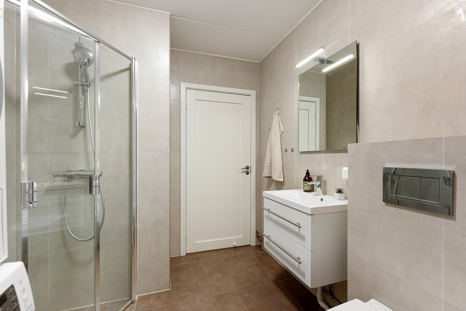 Badet har innredning med nedfelt servant, veggmontert toalett, svingbare dusjvegger og opplegg for vaskemaskin. Galleribilde