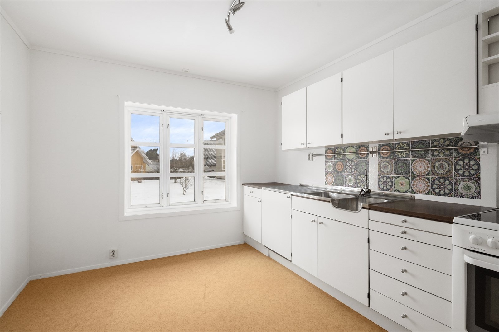 Lyst kjøkken med innredning bestående av over- og underskap samt et høyskap. Innredningen har slette fronter, laminert benkeplate og dobbel oppvaskkum med benkebeslag. Galleribilde