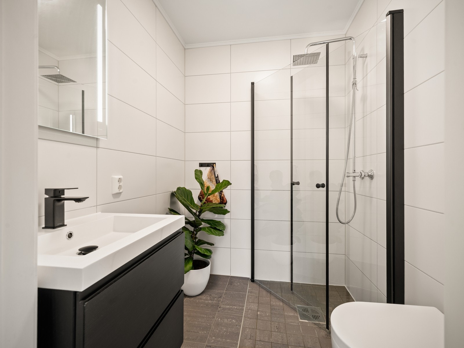 Flislagt bad med behagelig gulvvarme, utstyrt med vegghengt toalett, dusjhjørne med glassvegger og baderomsinnredning med servant og speil. Galleribilde