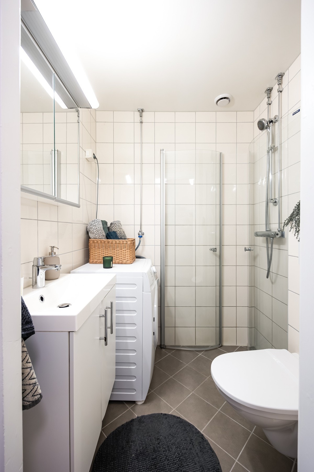 Flislagt baderom i nøytrale farger, med varmekabler og opplegg for vaskemaskin Galleribilde