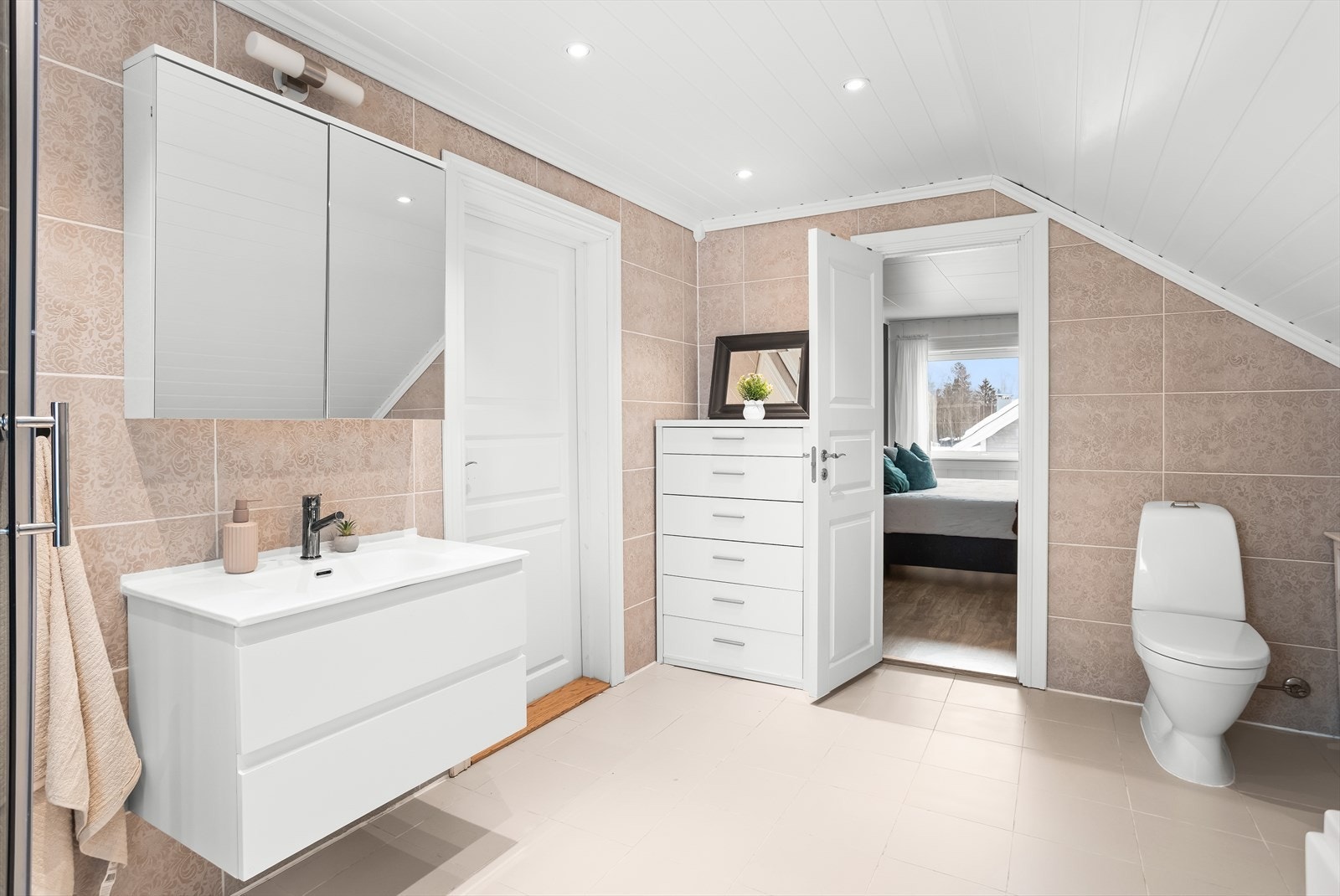 Badet har varme i gulvet for ekstra komfort, og er flislagt med hvite gulvfliser og beige veggfliser. Galleribilde