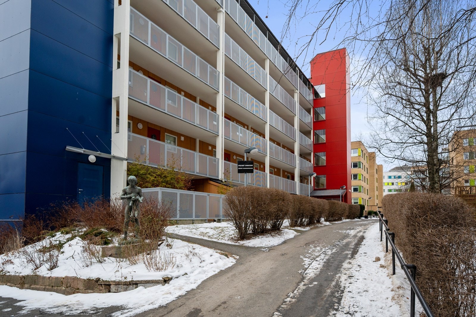 Felles gangvei foran bygningen med asfaltert sti, skulptur og busker. Galleribilde