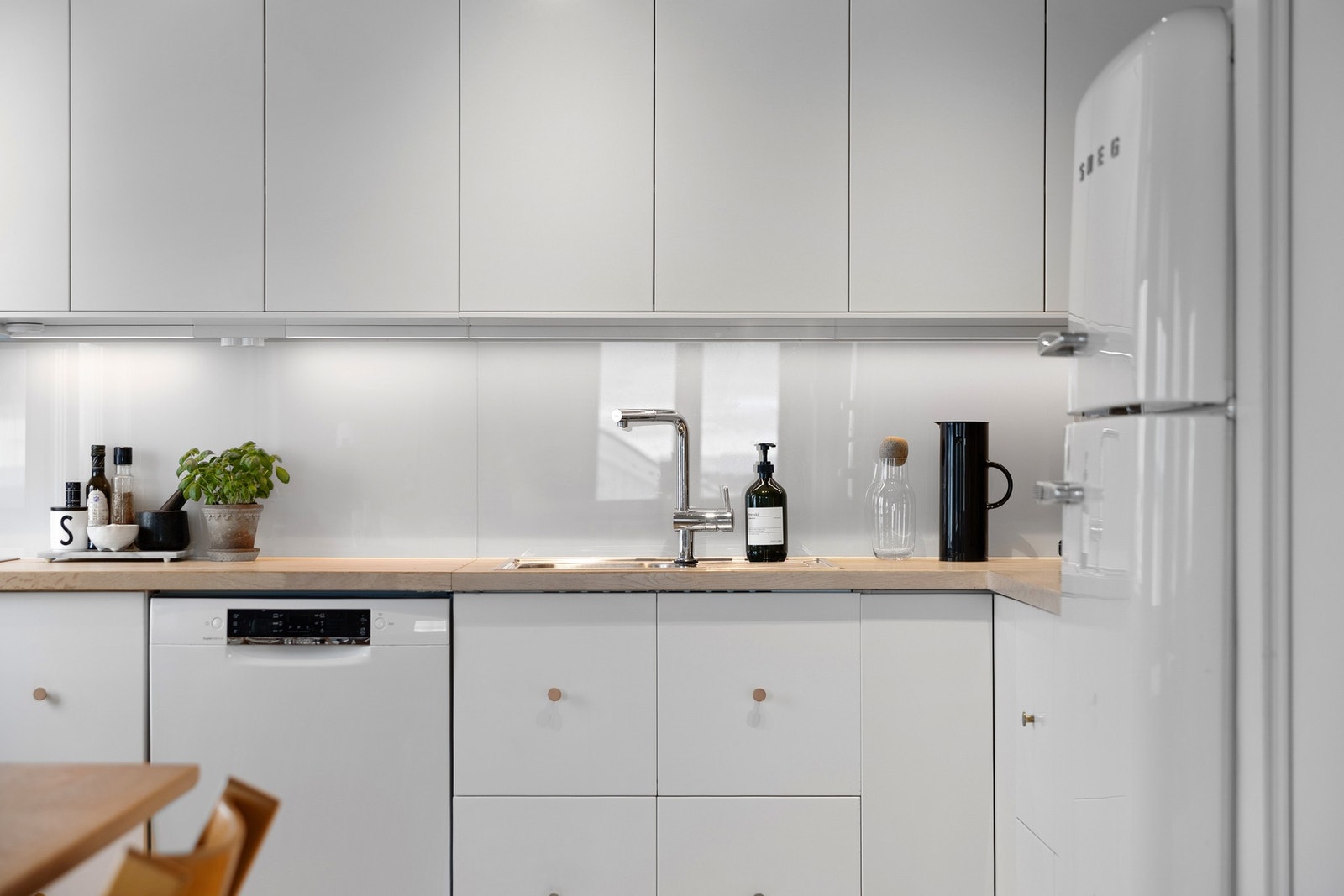 Pent kjøkken med lyse fronter, glassplater på vegg og benkeplate i tre. Galleribilde