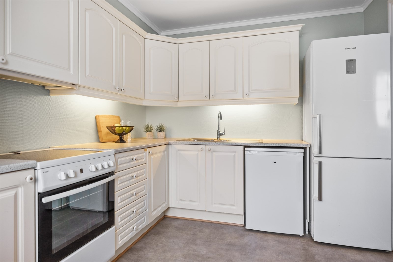 Her er det rikelig med både benkeplass og skapplass, noe som gir gode arbeidsforhold og effektiv oppbevaring. Løsningen legger til rette for en ryddig og oversiktlig kjøkkenhverdag, samtidig som det er god plass til matlaging for både hverdag og selskap. Galleribilde