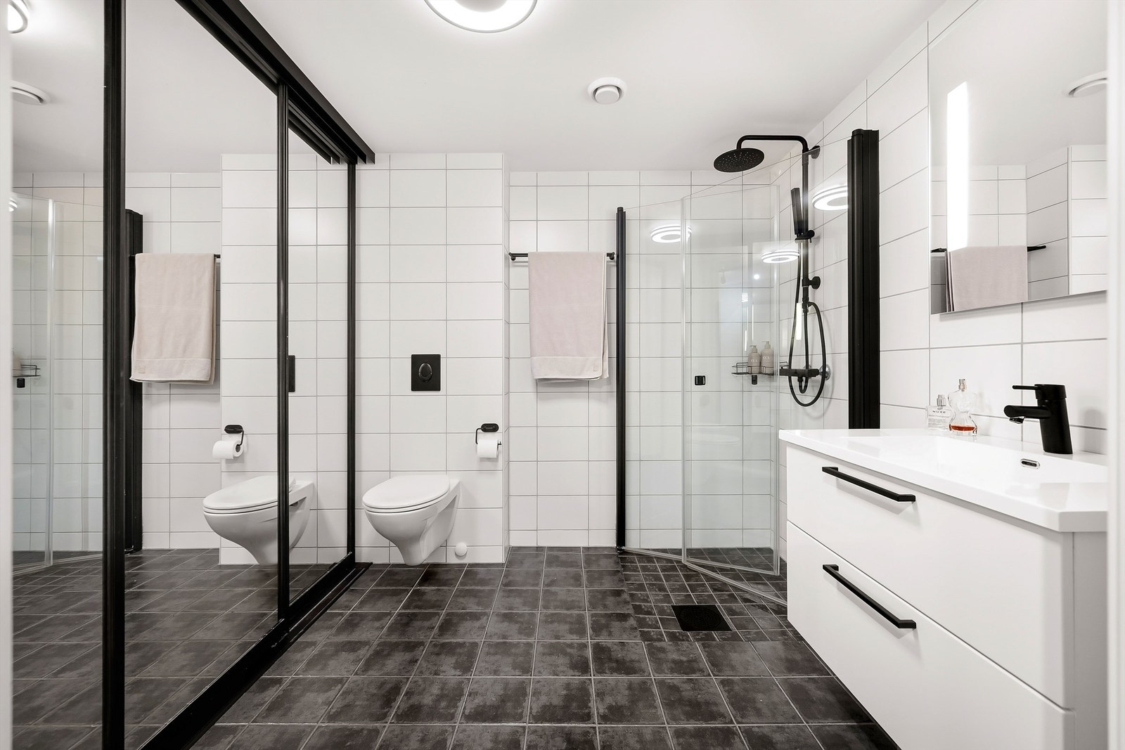 Badet har flislagt gulv med varmekabler, vegghengt toalett og dusj med innfellbare glassdører. Galleribilde