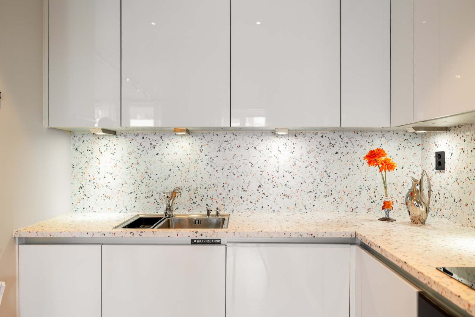 Nye hvitevarer i 2025 - Electrolux platetopp, stekeovn, kombiskap og Miele oppvaskmaskin. Under overskapene er det belysning og over kokesonen er det ventilator med avtrekk via sentralt avtrekksanlegg i bygget. Galleribilde