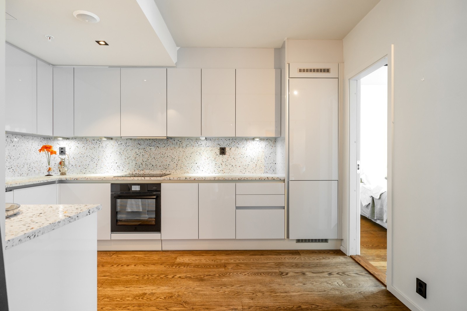 Kjøkkenet ligger i en delvis åpen løsning mot stuen og har en moderne innredning med lyse, glatte fronter og lys laminatbenkeplate. Galleribilde