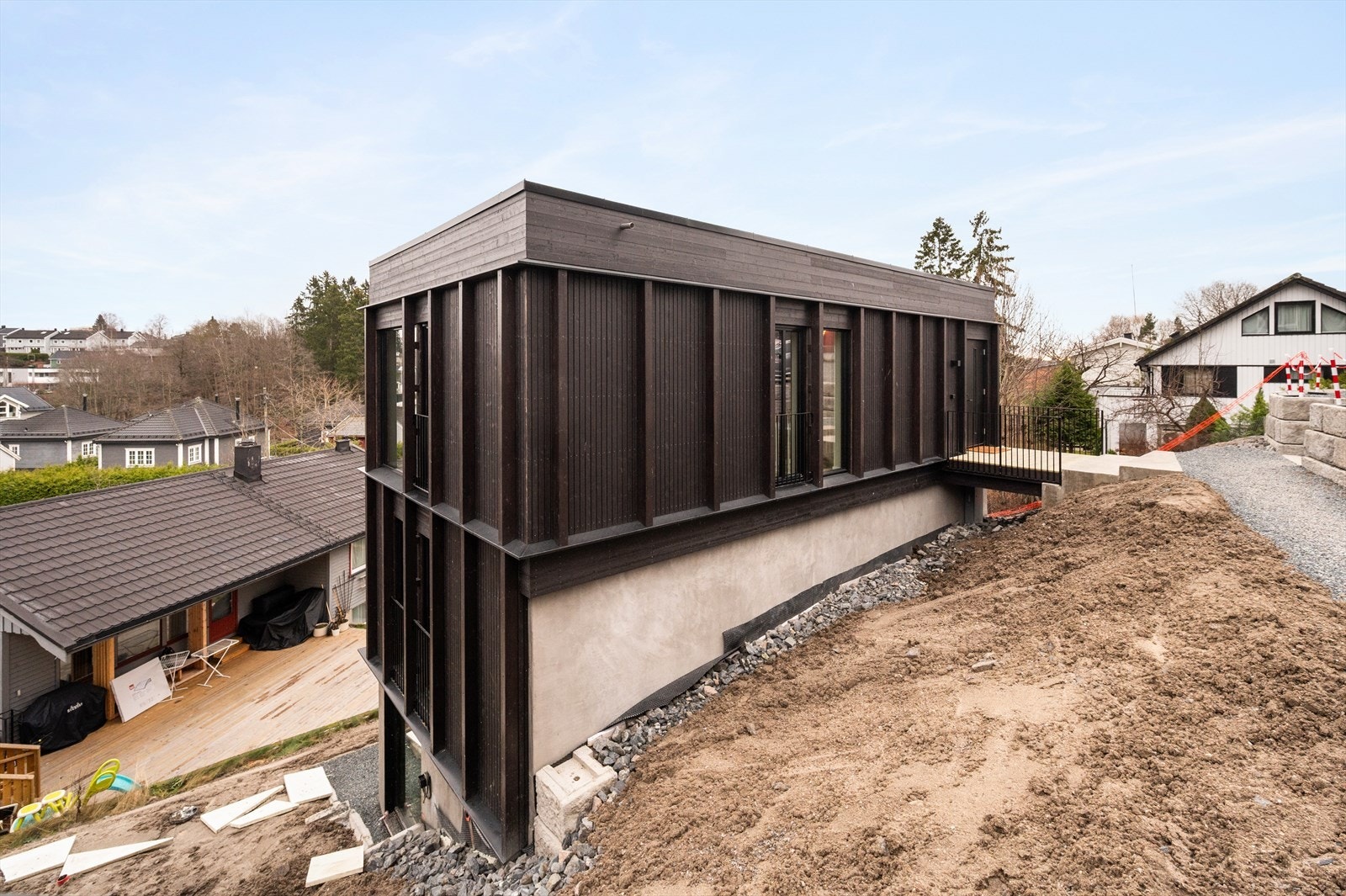 Fasade og inngangsparti. Boligen har adkomst via gangbro og inn til 2. etasje. Fasaden er systematisk inndelt med vertikale elementer som bryter volumene opp på en tilforlatelig måte. Galleribilde