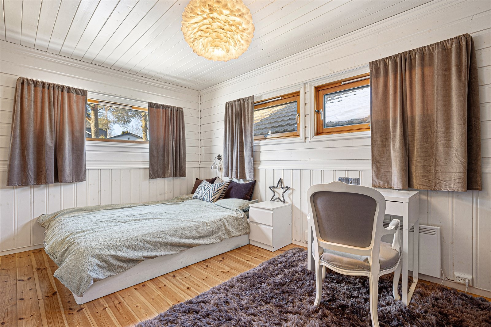 Det største soverommet i 1. etg har tregulv og brystpanel på veggene, kombinert med malt panel i himlingen som gir et lyst og moderne uttrykk. Med sine 14 m² og flere store vinduer får rommet rikelig naturlig lys og en luftig romfølelse. Galleribilde