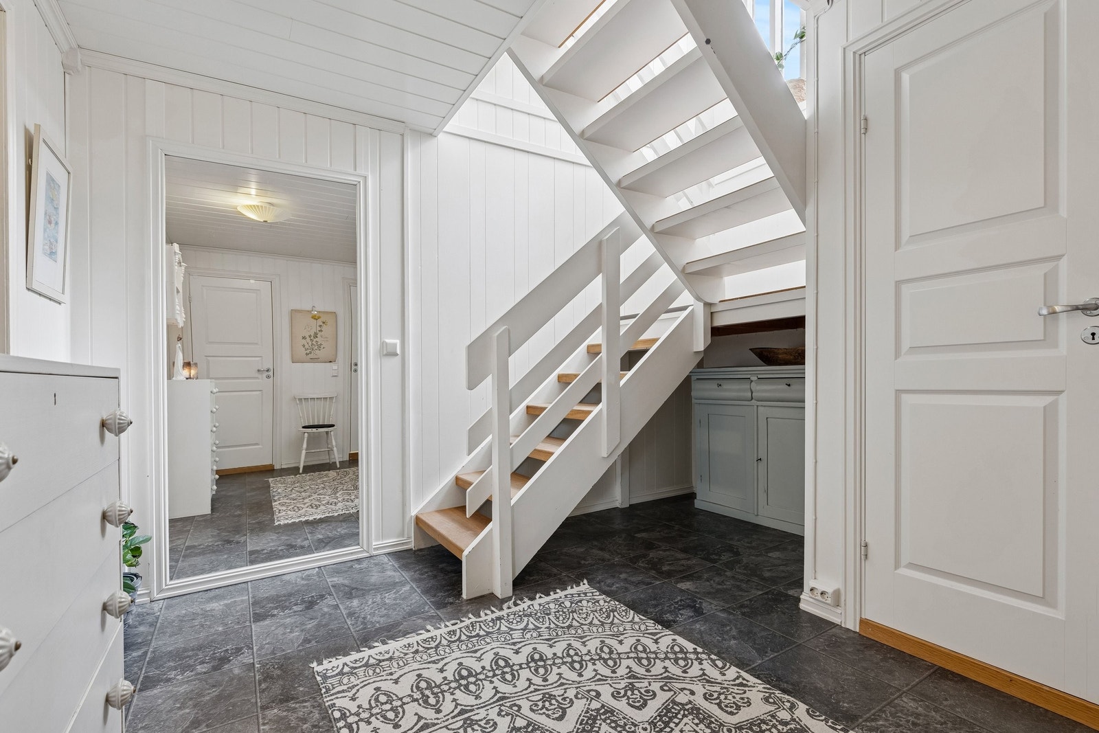 Fra en romslig hall leder trappen opp til hovedetasje. Her får man inn rikelig med lys fra stort vindu i trappeløpet. Galleribilde