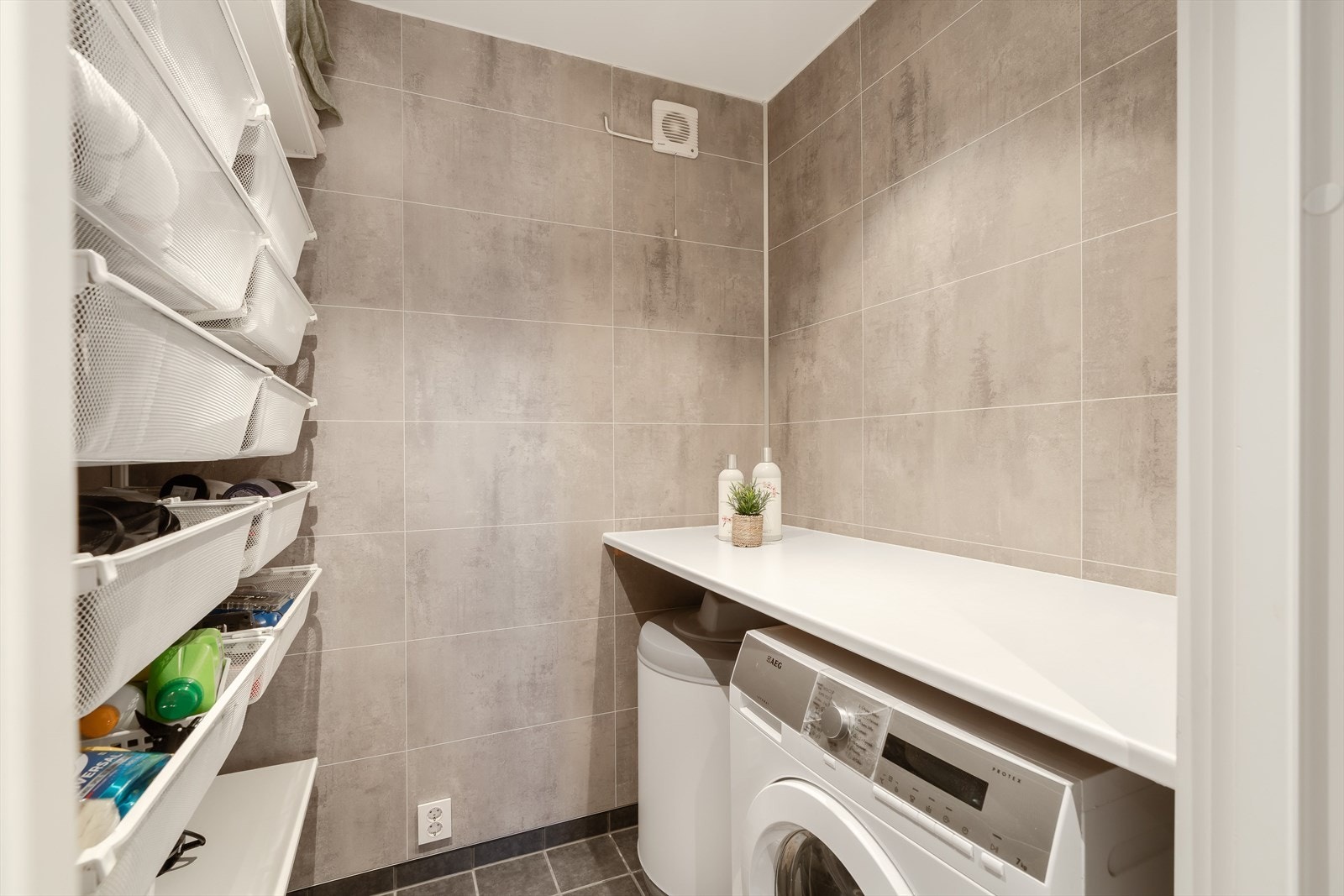 Flislagt vaskerom med opplegg for vaskemaskin. Her er det etablert baderomsvifte og det er godt med lagringsplass. Galleribilde