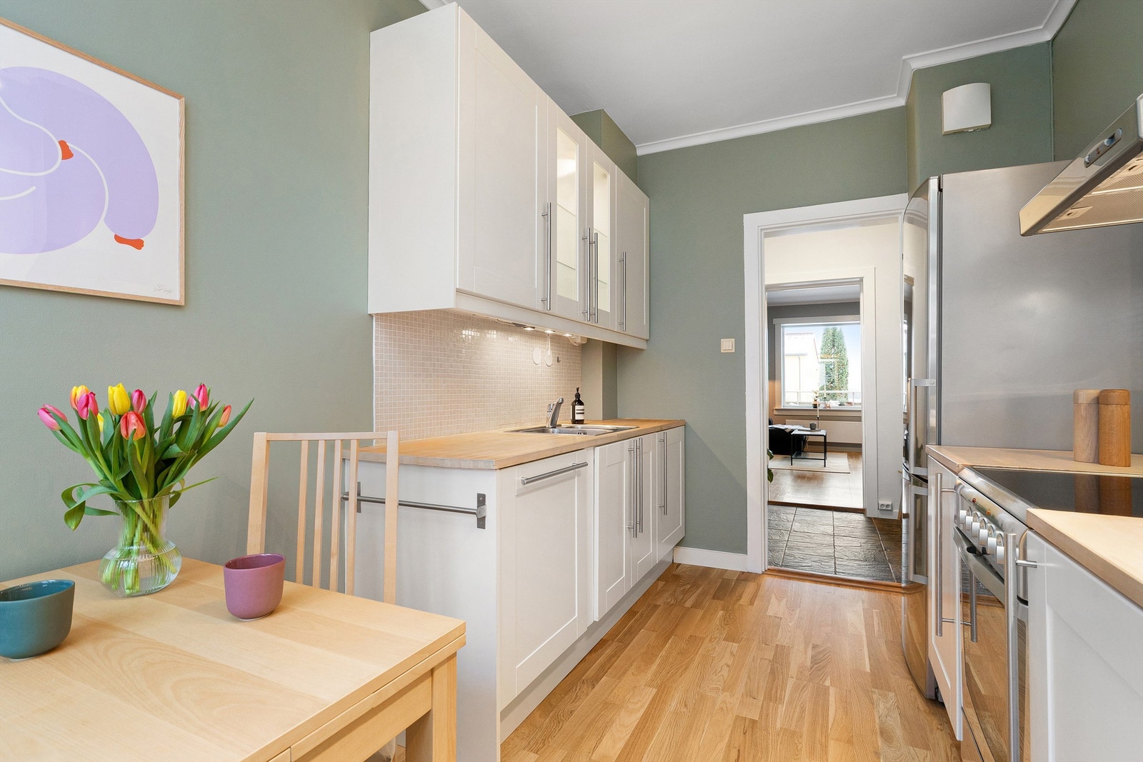 Tidløs kjøkkeninnredning med lyse profilerte fronter og benkeplate i tre, samt integrert oppvaskmaskin. Galleribilde