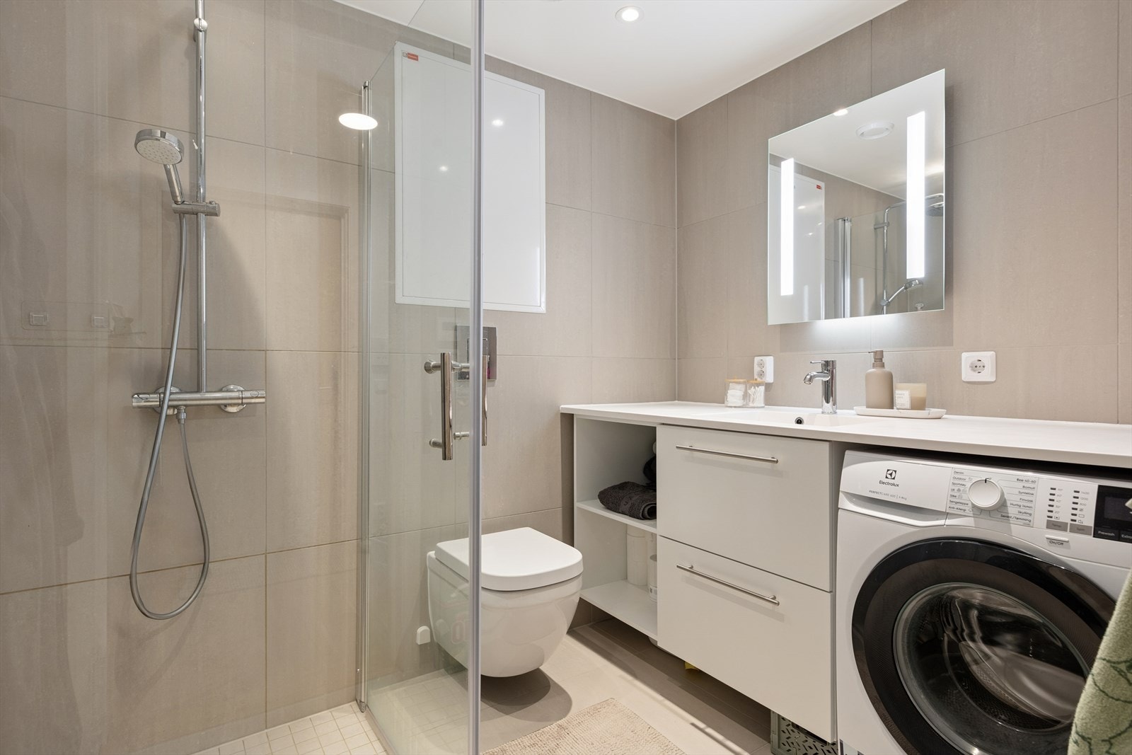 Bad (4,1 m²) utstyrt med dusjvegger av glass og dusjgarnityr på vegg, vegghengt toalett og innredning med servant. Opplegg for vaskemaskin. Galleribilde