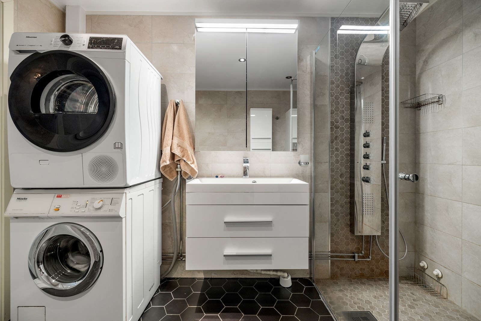 Badet har flislagte gulv og veggflater. Innredning bestående av benkeskap, veggskap og høyskap med slette fronte, servant, dusj med innfellbare dører, vegghengt toalett med innebygd sisterne Galleribilde