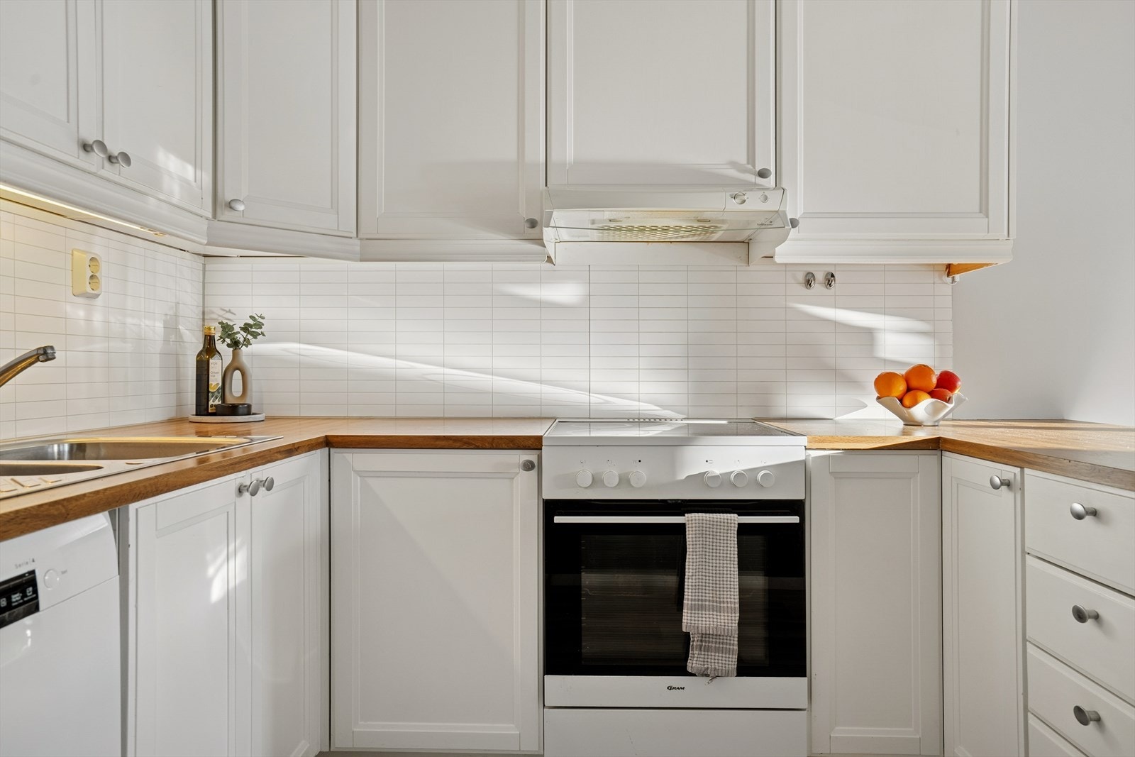 Innredningen har profilerte fronter og er godt utbygget med skapplass og benkplass for matlaging og tilberedning - Mellom benkeplate og overskap er det montert backsplash som både beskytter veggen og gir et helhetlig preg Galleribilde