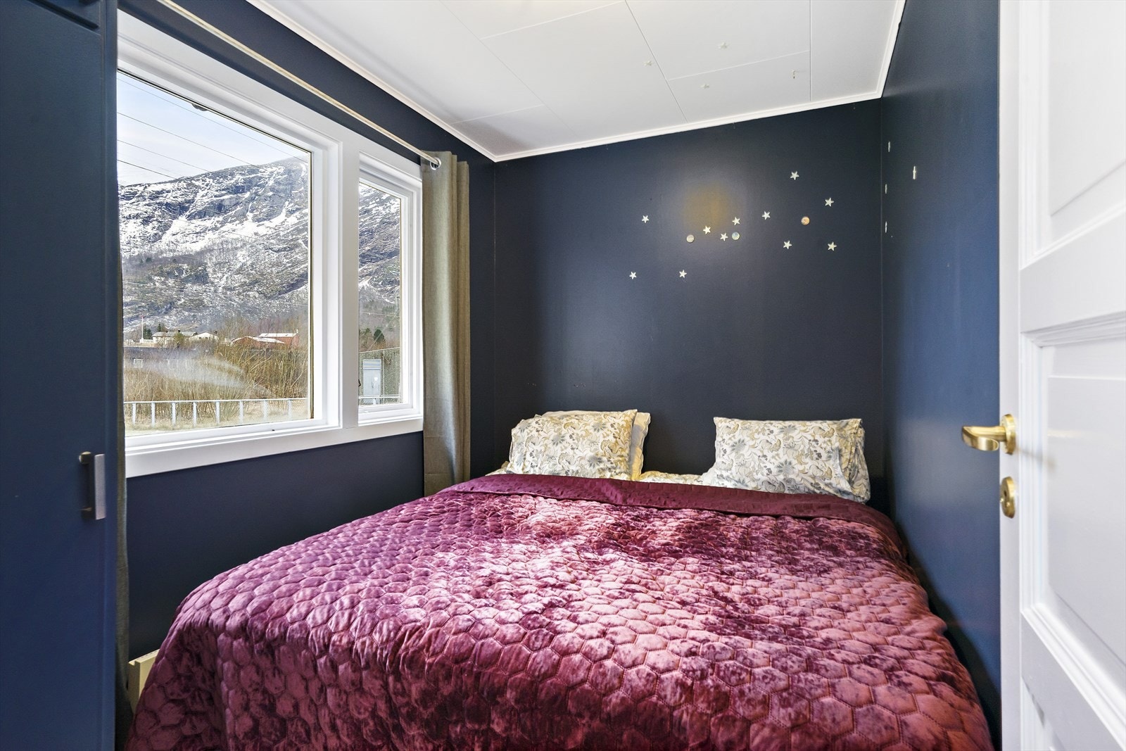 Soverom 1 med store vinduer og utsikt mot fjellene. Veggene er kledd med malte plater. Galleribilde