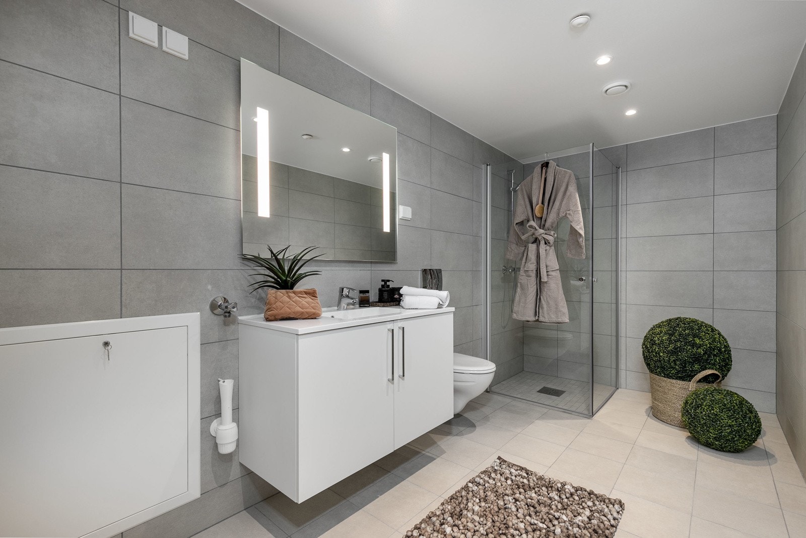 Delikat flislagt bad med vegghengt toalett, dusjsone med innfellbare dører samt servant med skapinnredning. Galleribilde