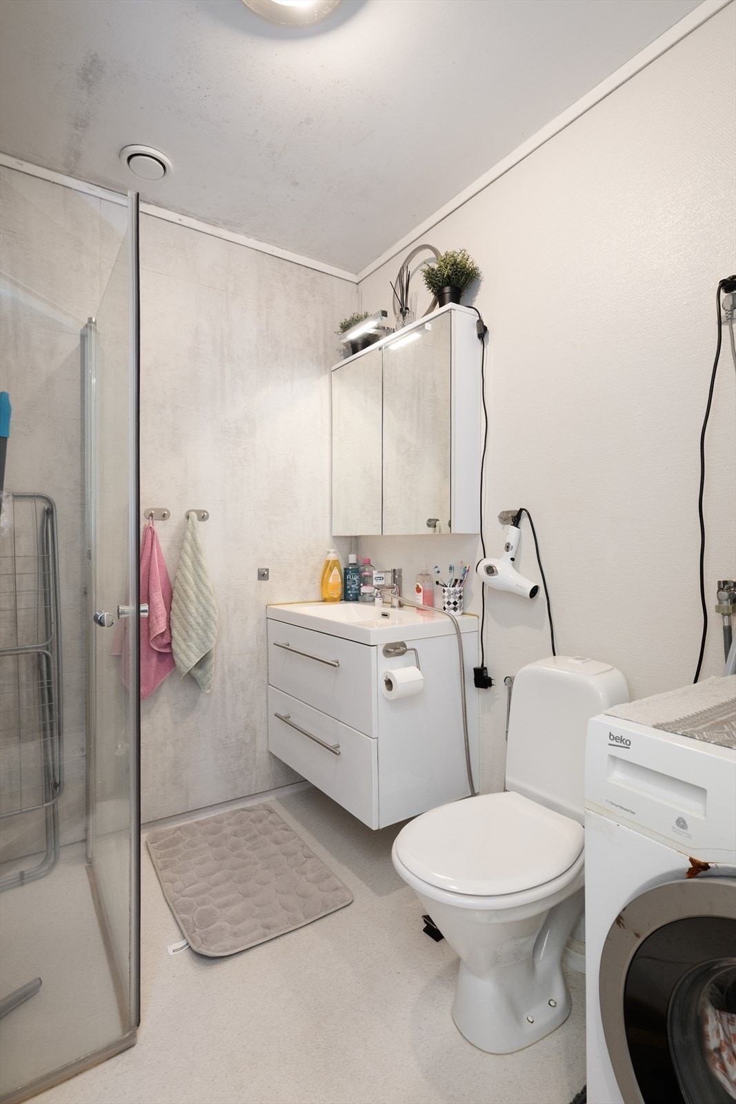 Lyst baderom i 2. etasje, med varmekabler i gulv, gulvmontert toalett og dusjnisje med glassvegger. Lys servantinnredning og opplegg for vaskemaskin. Galleribilde