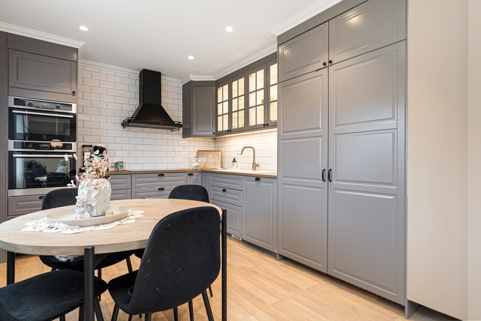 Kjøkkeninnredning med profilerte, malte skapfronter og med glass og med takhøye skap | benkeplater av laminat med nedfelt vask og platetopp | integrert mikroovn, komfyr, ventilator, oppvaskmaskin og kjøle- og fryseskap Galleribilde