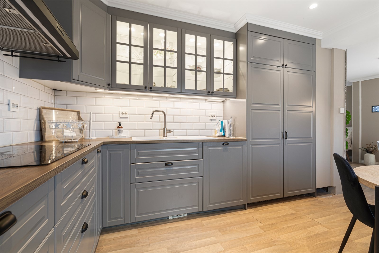 Kjøkkeninnredning med profilerte, malte skapfronter og med glass og med takhøye skap | benkeplater av laminat med nedfelt vask og platetopp | integrert mikroovn, komfyr, ventilator, oppvaskmaskin og kjøle- og fryseskap Galleribilde