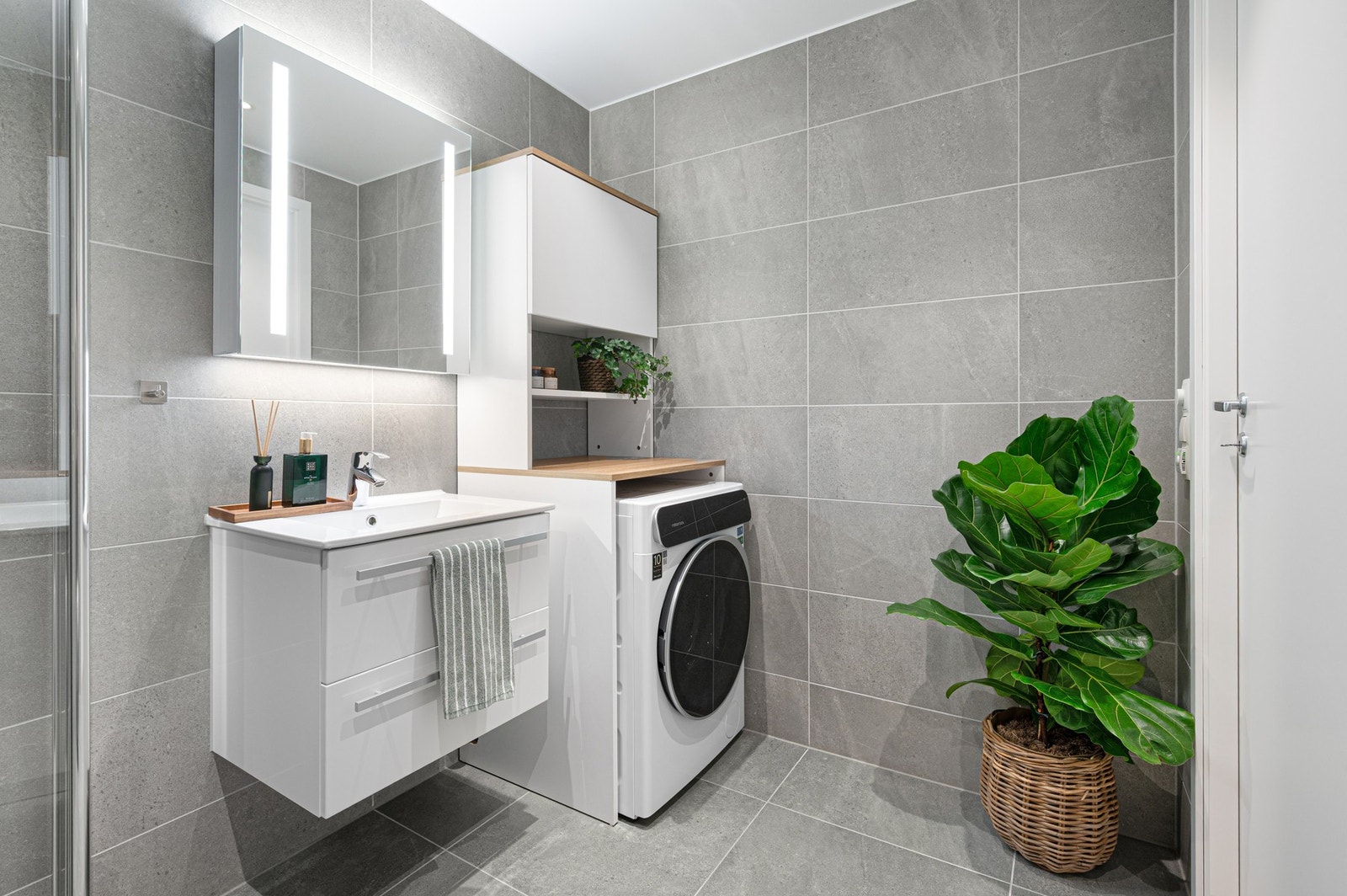 Badet er innredet med dusj med innfellbare dører i glass, veggmontert WC, kran og avløp for vaskemaskin, servant med underskap og speil. Galleribilde