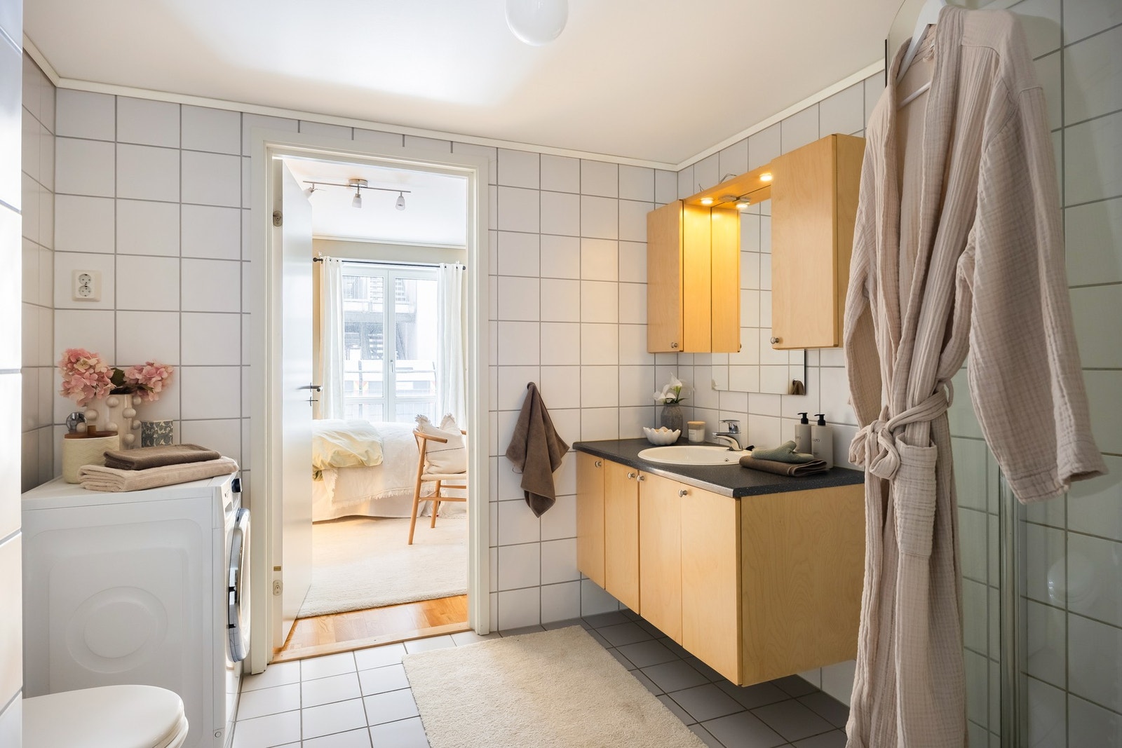 Flislagt bad med nøytrale flisvalg, romslig baderomsinnredning, opplegg for vaskemaskin, vegghengt toalett og dusjhjørne med innfellbare dører. Galleribilde